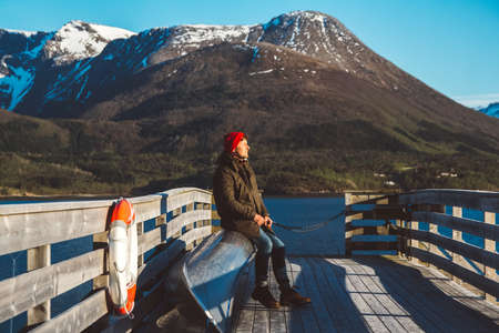 Traveler man is standing in the middle of a forest with a guitar on background of mountains and lake. Place for text or advertising. Shoot from the back.の写真素材