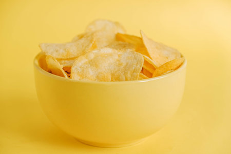 Potato chips in a yellow bowl on a yellow background. Copy, empty space for text.