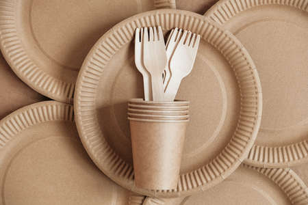 Wooden forks and paper cups with plates on kraft paper background. Eco friendly disposable tableware. Also used in fast food, restaurants, takeaways, picnics. Top view. Copy, empty space for text.の写真素材