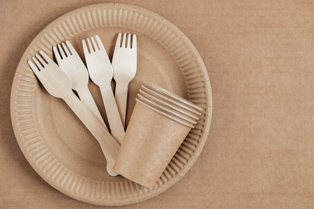 Wooden forks and paper cups with plates on kraft paper background. Eco friendly disposable tableware. Also used in fast food, restaurants, takeaways, picnics. Top view. Copy, empty space for text.の写真素材