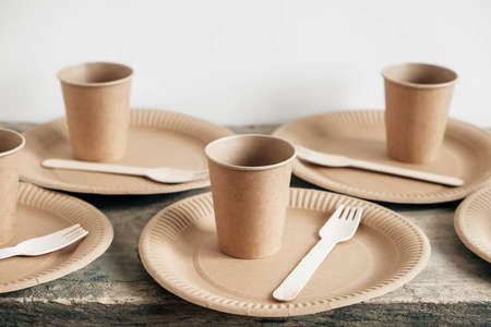 Wooden forks and paper cups with plates on wooden background. Eco friendly disposable tableware. Also used in fast food, restaurants, takeaways, picnics. Top view. Copy, empty space for text.の写真素材