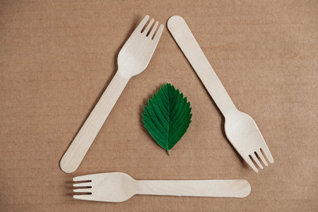 Wooden forks and paper cups with plates on wooden background. Eco friendly disposable tableware....