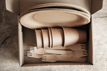 Wooden forks and paper cups with plates on wooden background. Eco friendly disposable tableware....