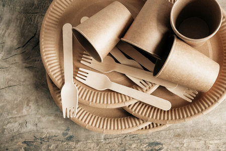 Wooden forks and paper cups with plates on wooden background. Eco friendly disposable tableware. Also used in fast food, restaurants, takeaways, picnics. Copy, empty space for text.の写真素材