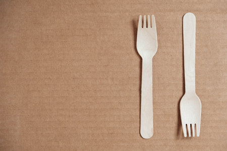 Wooden forks on a cardboard background. Eco friendly disposable tableware. Top view. Copy, empty...