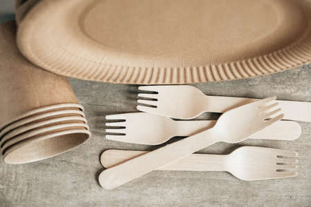 Wooden forks and paper cups with plates on wooden background. Eco friendly disposable tableware. Also used in fast food, restaurants, takeaways, picnics. Top view. Copy, empty space for text.の写真素材