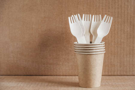 Wooden forks and paper cups with plates on wooden background. Eco friendly disposable tableware. Also used in fast food, restaurants, takeaways, picnics. Top view. Copy, empty space for text.の写真素材