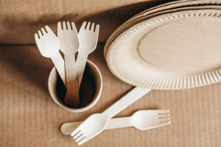 Wooden forks and paper cups with plates on wooden background. Eco friendly disposable tableware. Also used in fast food, restaurants, takeaways, picnics. Top view. Copy, empty space for text.の写真素材