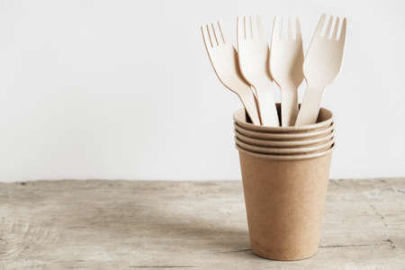 Wooden forks and paper cups with plates on wooden background. Eco friendly disposable tableware. Also used in fast food, restaurants, takeaways, picnics. Top view. Copy, empty space for text.の写真素材