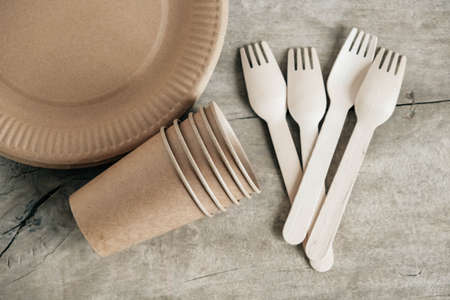 Wooden forks and paper cups with plates on wooden background. Eco friendly disposable tableware. Also used in fast food, restaurants, takeaways, picnics. Top view. Copy, empty space for text.の写真素材