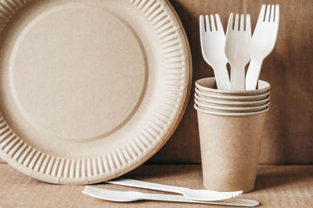 Wooden forks and paper cups with plates on kraft paper background. Eco friendly disposable tableware. Also used in fast food, restaurants, takeaways, picnics. Top view. Copy, empty space for text.の写真素材
