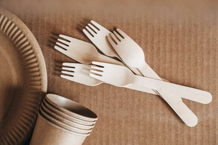 Wooden forks and paper cups with plates on kraft paper background. Eco friendly disposable tableware. Also used in fast food, restaurants, takeaways, picnics. Top view. Copy, empty space for text.の写真素材