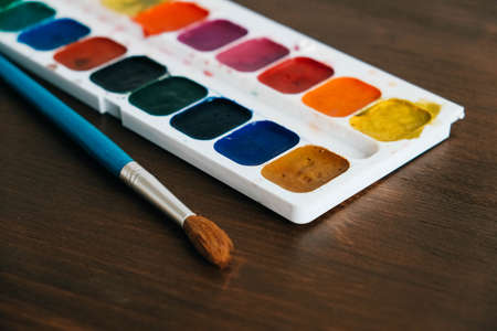 Set of watercolor paints with a brush for painting on a dark wooden background. Top view. Copy, empty space for text.の写真素材