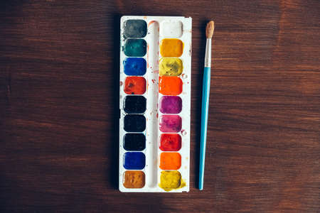 Set of watercolor paints with a brush for painting on a dark wooden background. Top view. Copy, empty space for text.の写真素材