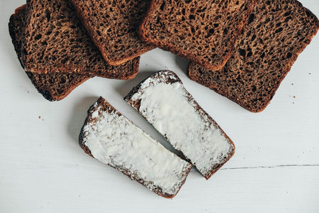 Sliced of brown bread with butter on a white wooden background. Top view. Copy, empty space for...