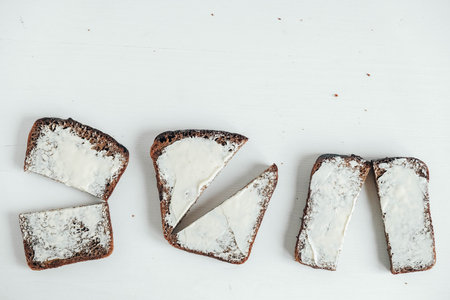 Sliced of brown bread with butter on a white wooden background. Top view. Copy, empty space for...