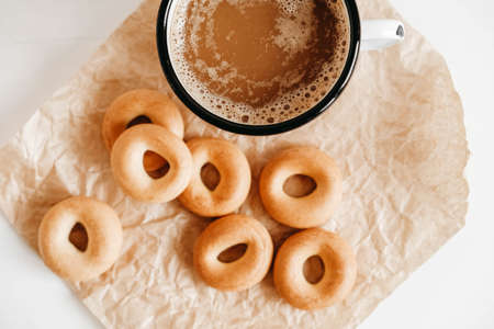 Metal mug with hot drink and mini round bagels on a white wooden background. Top view. Copy, empty space for text.の写真素材