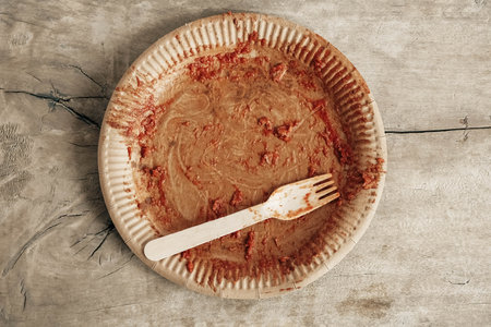 Dirty from food disposable paper utensils on a wooden background. Wooden fork and paper plate on wooden background. Eco friendly disposable tableware. Top view. Copy, empty space for text.の写真素材