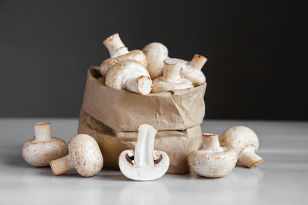 Mushrooms champignons in paper bag on a white wooden table. Place for text or advertising.の写真素材