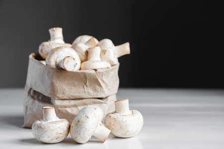 Mushrooms champignons in paper bag on a white wooden table. Place for text or advertising.の写真素材