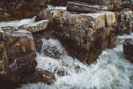 Stream of river among stones and rocks. Stream in stone bed, fast mountain river among rocks, water boils in eddies of current.の写真素材