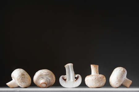 Mushrooms champignons lie in a row on a white table on a dark background. Place for text or advertising.の写真素材