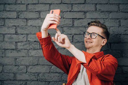 Portrait young man in shirt, jeans and glasses carrying a backpack and looking at smartphone while standing on a pink background. Copy, empty space for text.の写真素材