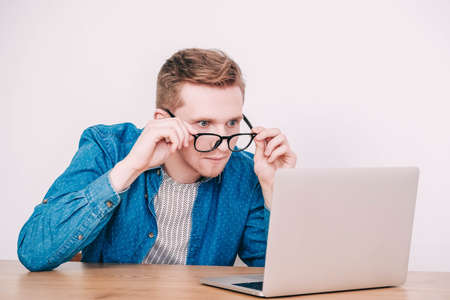Portrait young man in shirt, jeans and glasses carrying a backpack and looking at smartphone while standing on a pink background. Copy, empty space for text.の写真素材