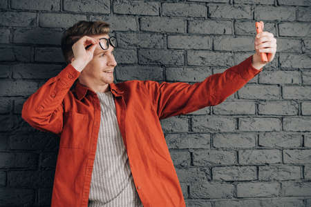 Portrait young man in shirt, jeans and glasses carrying a backpack and looking at smartphone while standing on a pink background. Copy, empty space for text.の写真素材