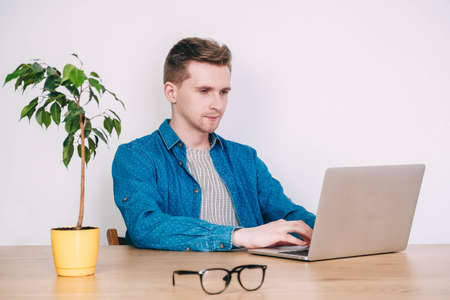Portrait young man in shirt, jeans and glasses carrying a backpack and looking at smartphone while standing on a pink background. Copy, empty space for text.の写真素材