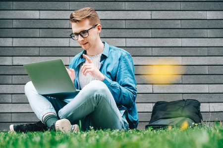 Young man in shirt and glasses he looks at the laptop in amazement and with a funny face sitting at the table on a white background. Funny face and amazement. Copy, empty space for text.の写真素材