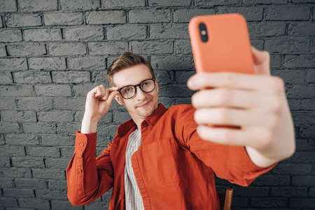 Young man in shirt and glasses he looks at the laptop in amazement and with a funny face sitting at the table on a white background. Funny face and amazement. Copy, empty space for text.の写真素材