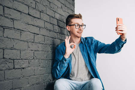 Young man in shirt and glasses he looks at the laptop in amazement and with a funny face sitting at the table on a white background. Funny face and amazement. Copy, empty space for text.の写真素材