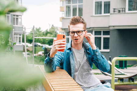 Young man in shirt and glasses he looks at the laptop in amazement and with a funny face sitting at the table on a white background. Funny face and amazement. Copy, empty space for text.の写真素材