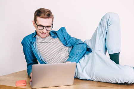 Young man in shirt and glasses he looks at the laptop in amazement and with a funny face sitting at...