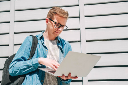Young man businessman in shirt, jeans and glasses sitting on green grass and using laptop computer...