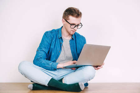 Young joyful man in shirt, jeans and glasses carrying a backpack and taking selfie photo on cellphone on a background of a pink wall. Copy, empty space for text.の写真素材