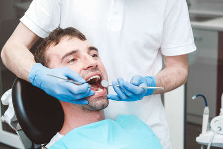 Dentist examines the teeth of a male patient on a dentist's chair. Copy, empty space for text.の写真素材