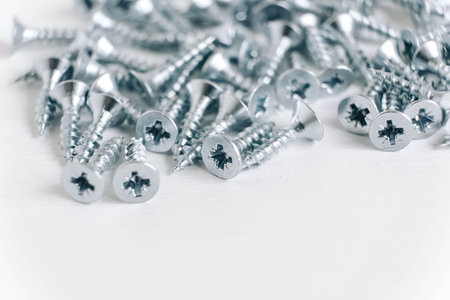 Metal tapping screws for wood on white wooden background. Construction equipment concept. Copy,...