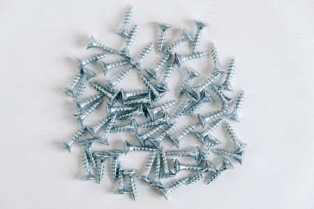 Metal tapping screws for wood on white wooden background. Construction equipment concept. Top view. Copy, empty space for text.の写真素材