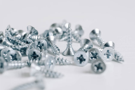 Metal tapping screws for wood on white wooden background. Construction equipment concept. Top view....