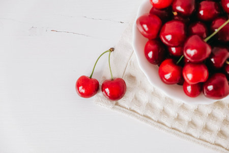 Fresh juicy red cherries in a white plate on the white wooden background. Top view. Copy, empty space for text.の写真素材