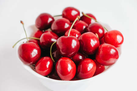 Fresh juicy red cherries in a white plate on the white wooden background. Copy, empty space for text.の写真素材