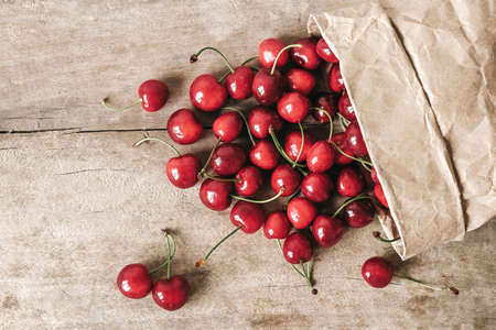 Fresh ripe cherries in a paper bag on wooden background. Top view. Copy, empty space for text.の写真素材