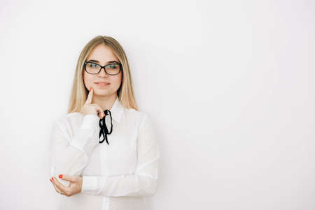 Beautiful blonde girl wears glasses stylish white shirt with a pensive face on a white wall background. Copy, empty space for text.の写真素材