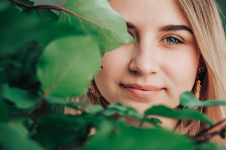 Portrait of a beautiful blonde girl with natural beauty in a green leaves trees. Copy, empty space for text.の写真素材