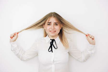 Shocked panic blonde woman dressed in stylish white shirt pulls her hands by her hair in despair and frustration. Copy, empty space for text.の写真素材