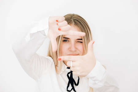 Young beautiful blonde woman wearing stylish white shirt making frame with her hands on a white wall background. Copy, empty space for text.の写真素材