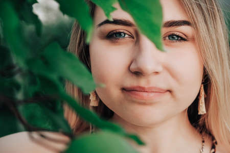 Portrait of a beautiful blonde girl with natural beauty in a green leaves trees. Copy, empty space for text.の写真素材