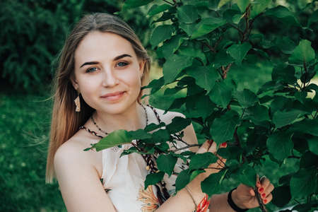 Portrait of a beautiful blonde girl with natural beauty in a green leaves trees. Copy, empty space for text.の写真素材
